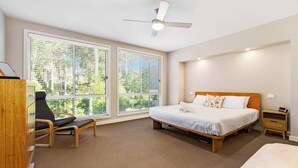 A bedroom with a bed, a desk, and a chair. There are large windows and a ceiling fan.