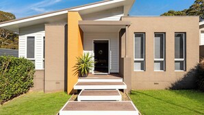 A modern two-story house with a flat roof, a front porch with steps, and a large potted plant.