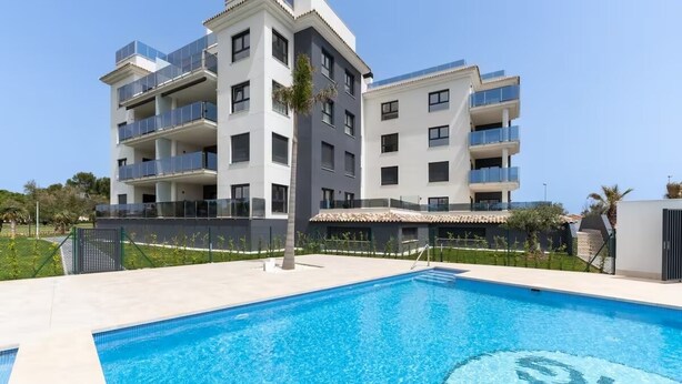 Ein modernes, mehrstöckiges Gebäude mit Balkonen, einem Swimmingpool und blauem Himmel.