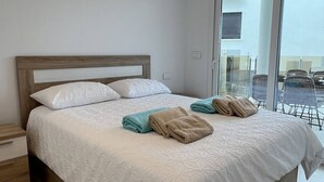 Ein ordentlich bezogenes Bett mit Holz Kopfteil, einem Nachttisch und Blick auf den Außenbereich durch eine Glastür.