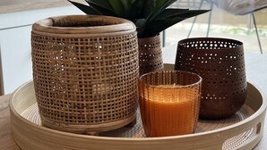 Ein runder Holztisch mit drei geflochtenen Behältern und einer Kerze.