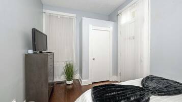A bedroom with a bed, a dresser, a television, a potted plant, and a door.