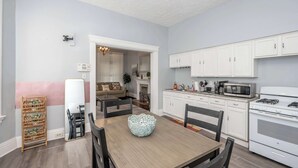 Un coin repas avec une table en bois, des chaises et un bol décoratif. La cuisine est équipée de meubles blancs et d’un four à micro-ondes.