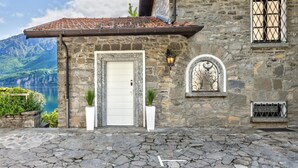 A stone building with a tiled roof, a white door, and a view of a lake and mountains.