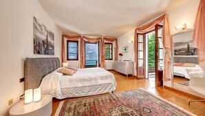 A bedroom with a bed, a nightstand, a dresser, and a large window with curtains.