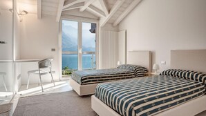 Une chambre avec deux lits, un bureau et une chaise, offrant une vue sur la mer et les montagnes.