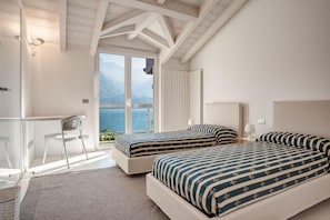 Ein Schlafzimmer mit zwei Betten, einem Schreibtisch und einem Stuhl, mit Blick auf das Meer und die Berge.