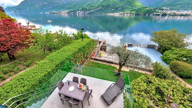 Une terrasse avec une table et des chaises donnant sur un lac et des montagnes.