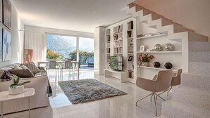 Un salon moderne comprenant un canapé, une table basse, un tapis, un meuble pour la télévision et un escalier.
