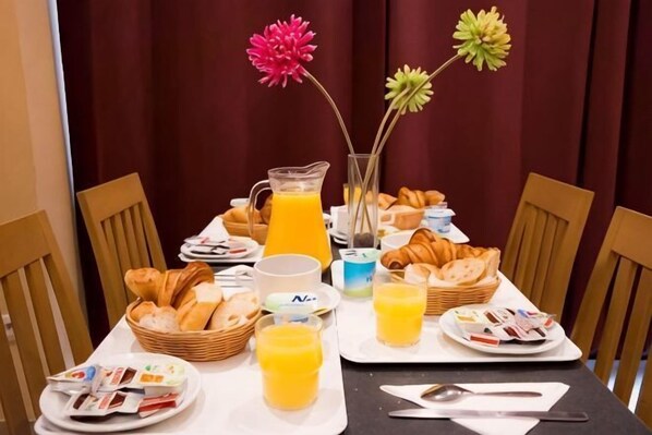 A breakfast table with croissants, juice, and pastries. - Hotel Audran (Paris)