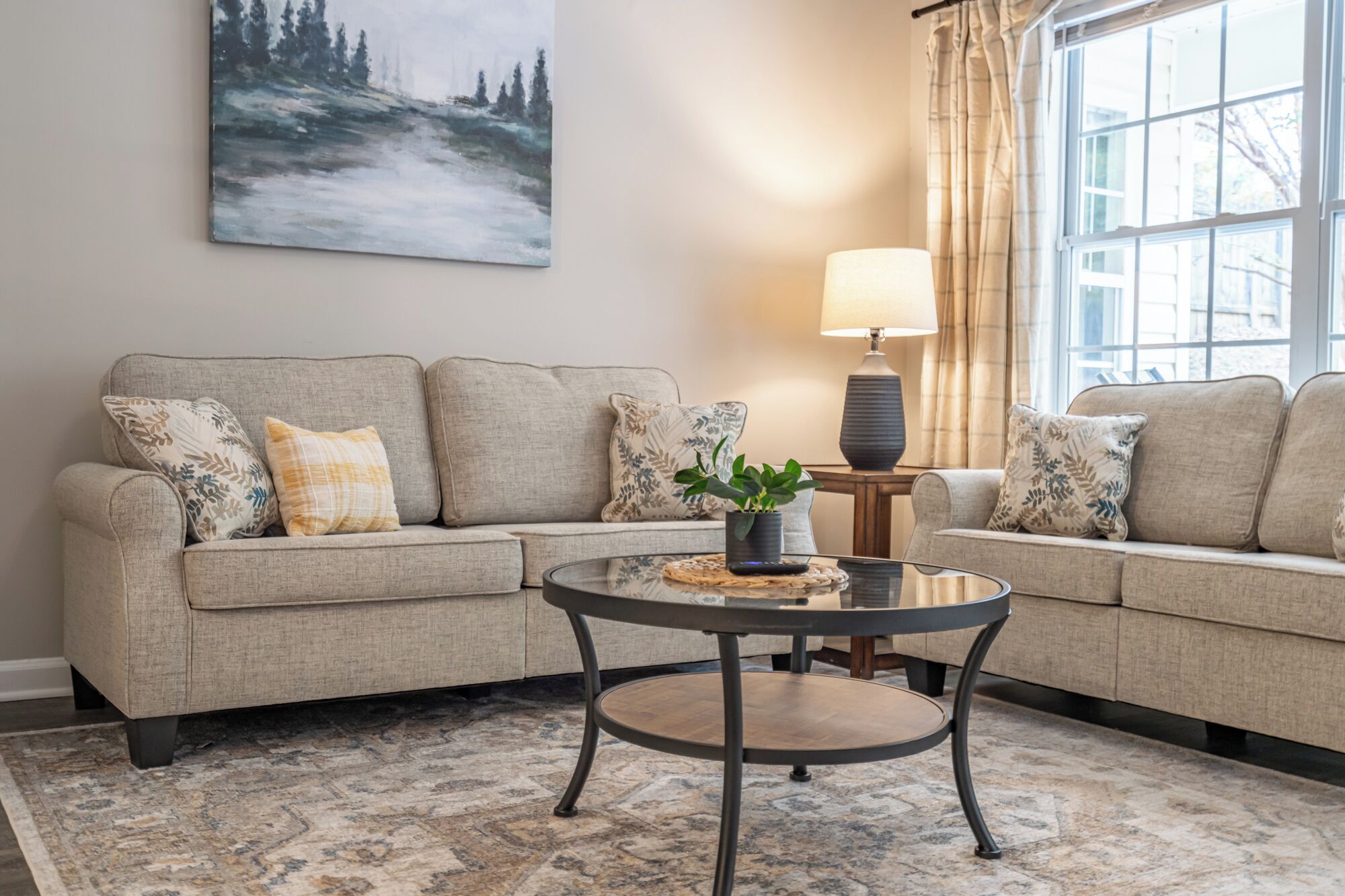 A living room with a beige sofa, a round coffee table, and a painting on the wall.