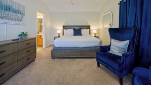 Une chambre à coucher avec un grand lit, une coiffeuse, un fauteuil bleu et un ventilateur de plafond.