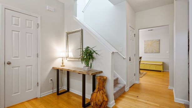 Un couloir avec une console en bois, un miroir, une plante en pot et un escalier menant à une autre pièce.