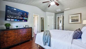 Une chambre à coucher comprenant un lit, une commode, un téléviseur fixé au mur et un ventilateur de plafond.