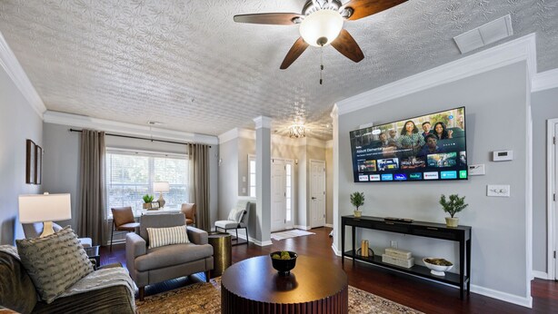 Un salon doté d’un ventilateur de plafond, d’un grand téléviseur à écran plat fixé au mur, d’une table basse et d’un canapé.