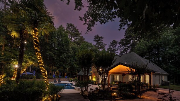 A house with a pool, surrounded by trees and decorated with string lights.