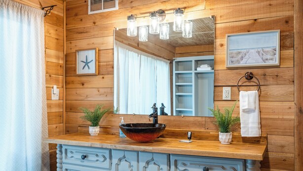 Un baño tipo cabaña de madera con un espejo grande, tocador de madera y dos plantas en macetas.