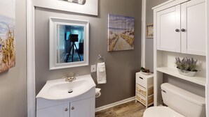 Un baño moderno con lavamanos, inodoro y mueble blancos, un espejo y un cuadro en la pared.