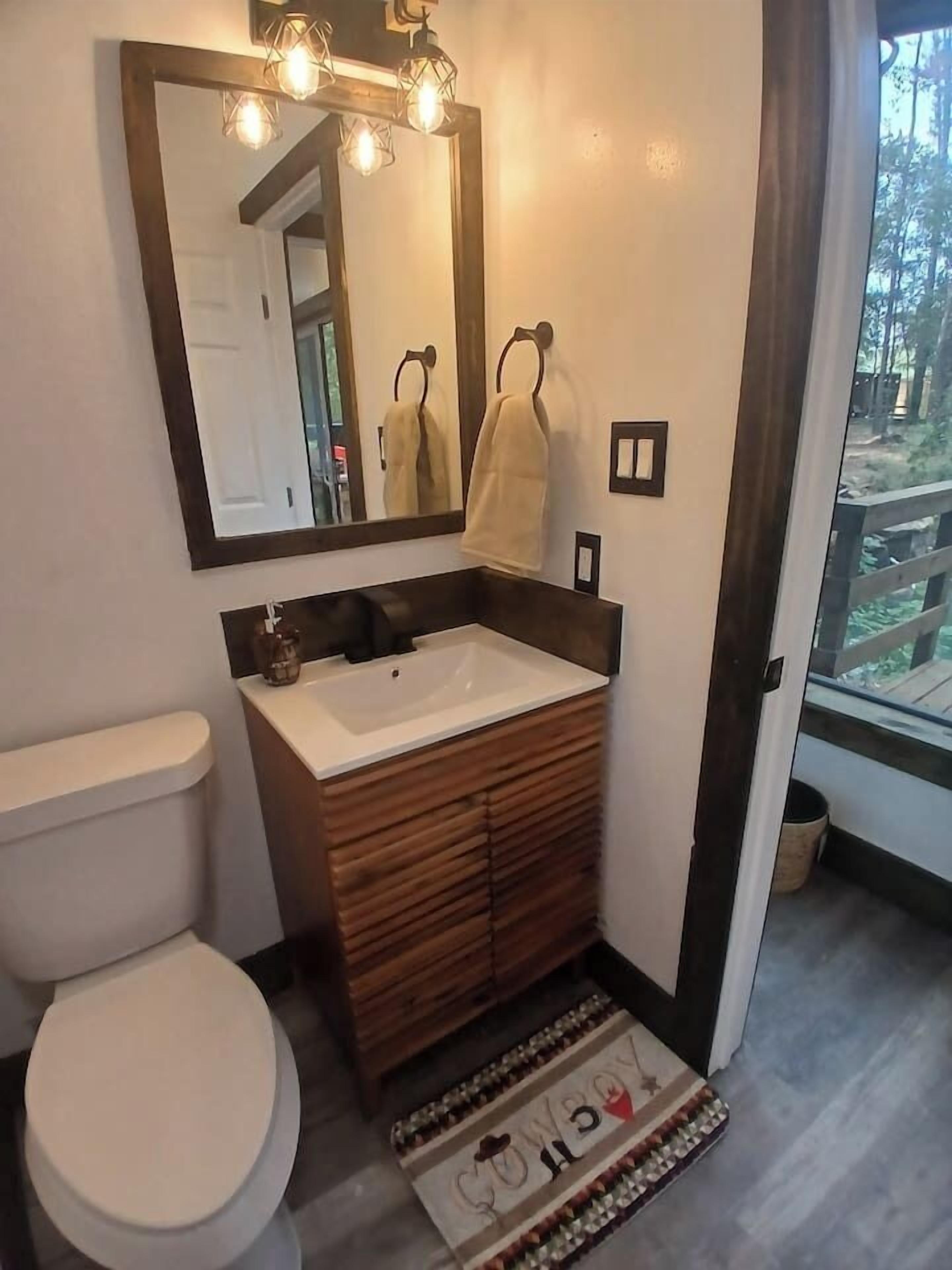 A bathroom with a white toilet, wooden vanity, and a mirror with lights.