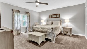 A bedroom with a bed, bedside tables, a ceiling fan, and a window with curtains.