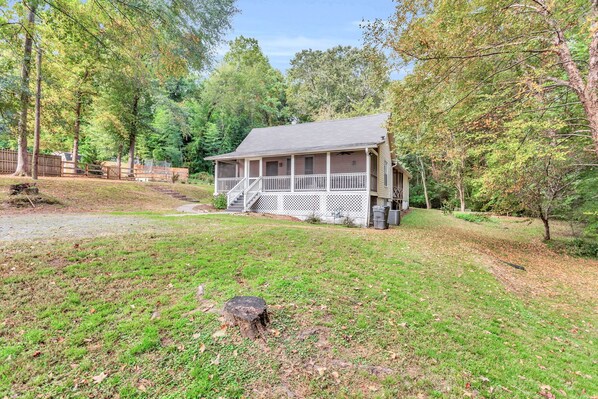 A cabin with a porch, surrounded by trees and a grassy yard.