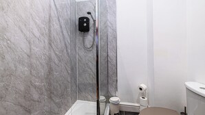 Un baño con ducha envuelta en vidrio, inodoro y cubo de basura.