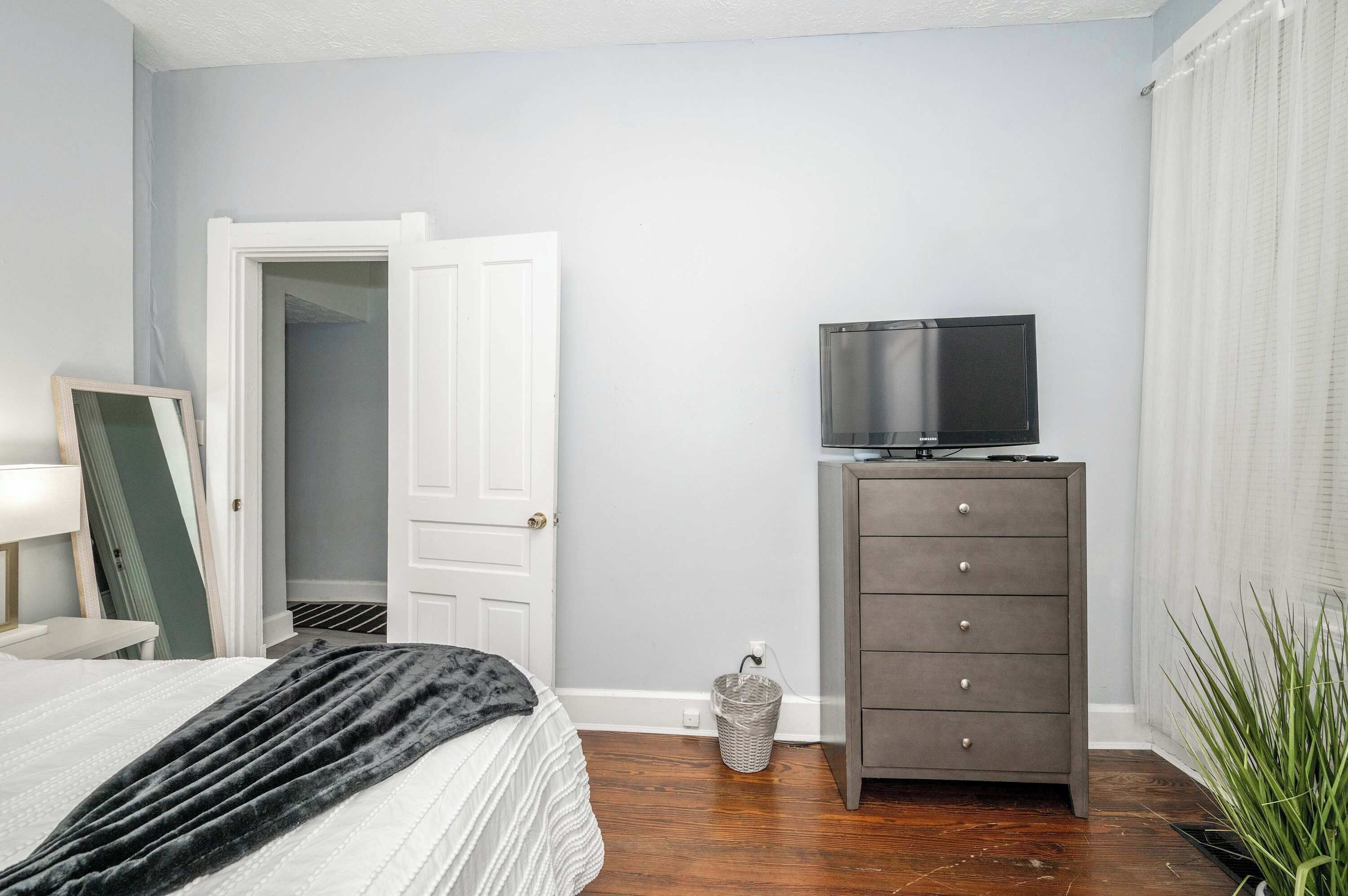 Une chambre à coucher comprenant un lit, une commode, un téléviseur et une porte donnant sur un placard.