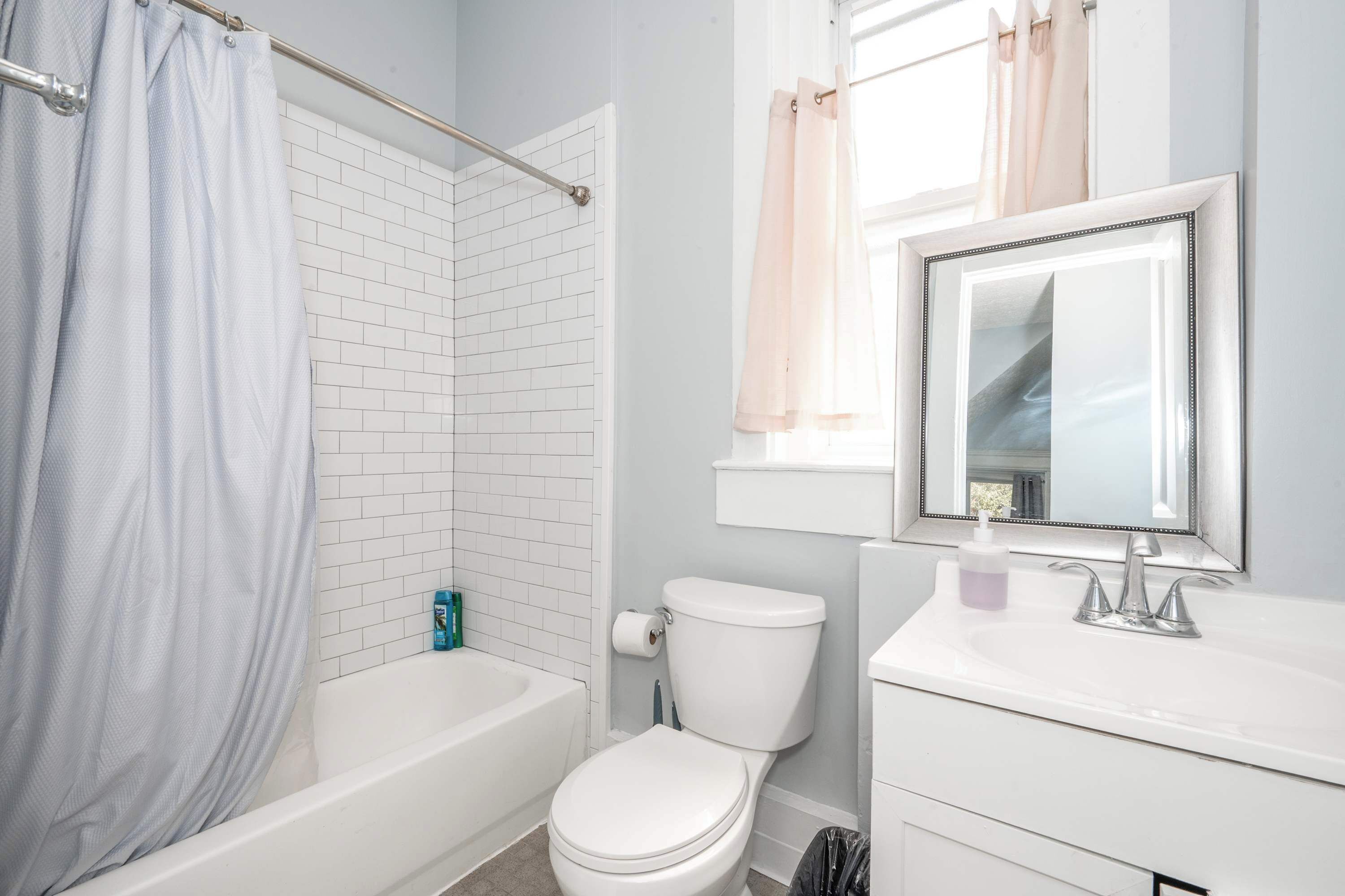 A bathroom with a white bathtub, a toilet, a sink with a mirror, and a shower curtain.