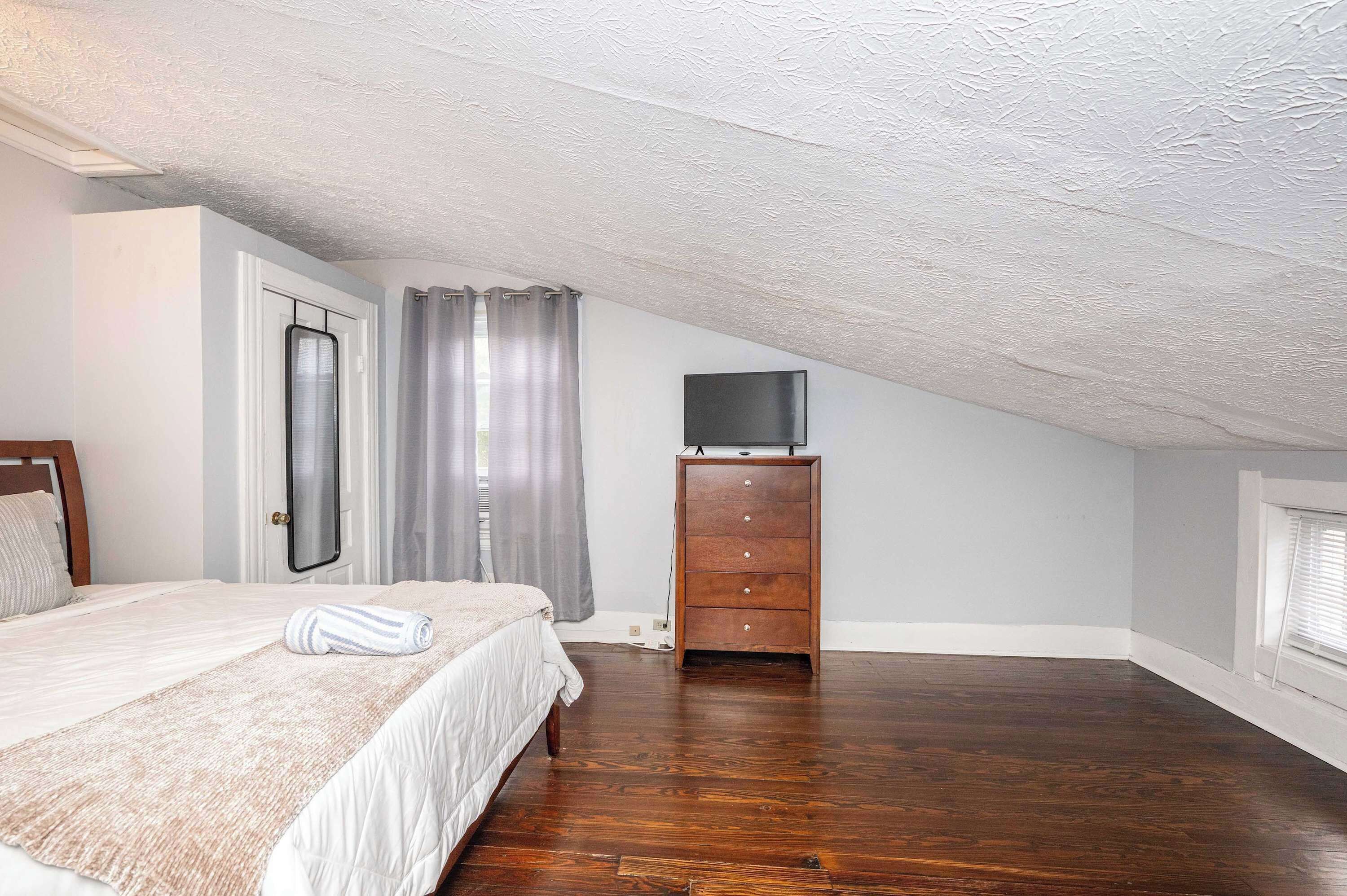 Une chambre à coucher avec un lit, une commode, un téléviseur et une fenêtre.