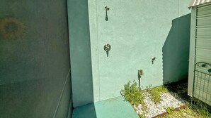 Un coin d’un bâtiment avec un mur vert à texture, une porte en métal dotée d’une poignée et une petite zone de végétation.