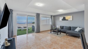 A modern living room with a grey sofa, a flat-screen TV, a coffee table, and a view of the outdoors. - Vacation Apartment 'Ocean View Costa Adeje' with Sea View, Private Terrace and Wi-Fi (Costa Adeje)