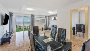A modern hotel room with a dining area, a flat-screen TV, a large mirror, and a view of the beach. - Vacation Apartment 'Ocean View Costa Adeje' with Sea View, Private Terrace and Wi-Fi (Costa Adeje)
