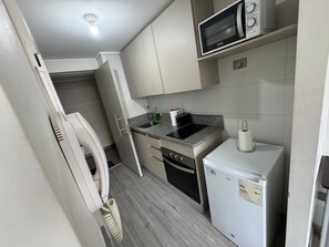 Una cucina compatta con forno a microonde, piccolo frigorifero, lavandino e piano cottura.