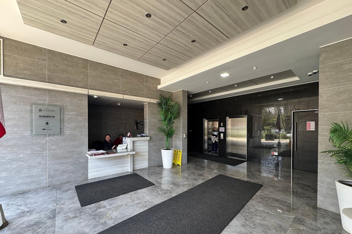 A modern reception area with a reception desk, a large potted plant, and a glass elevator.