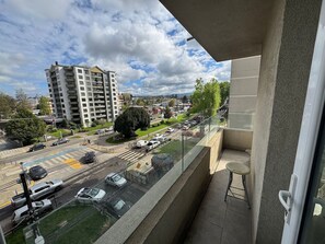 A balcony with a view of a busy street, a large tree, and a tall building in the background.