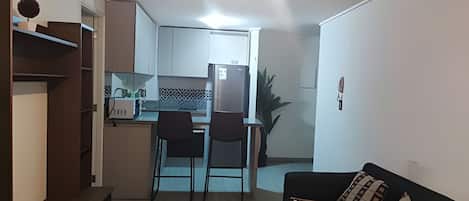Un espacio habitable compacto con kitchenette, comedor y zona de estar.