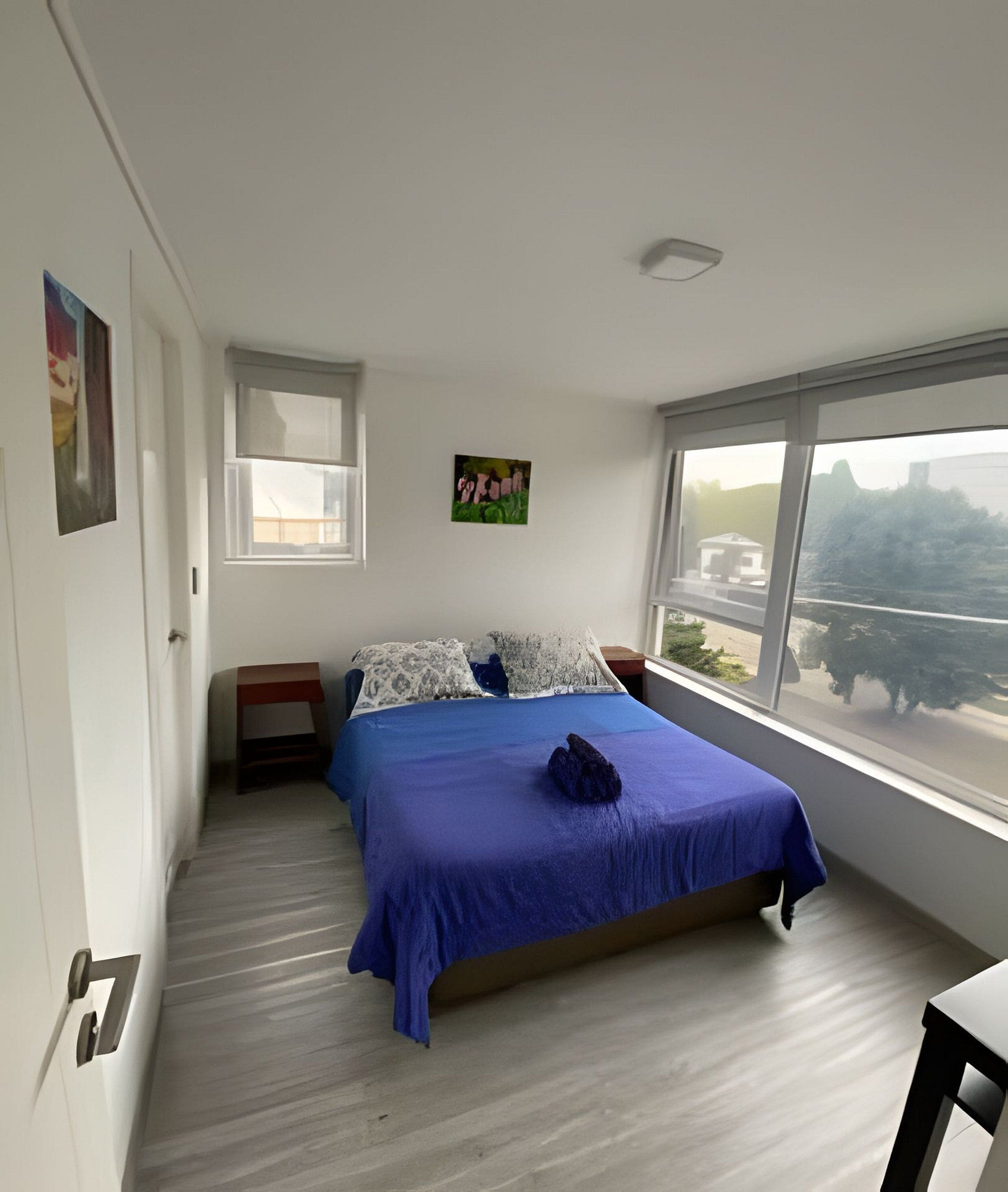 A bedroom with a large bed, a window, a painting, and a nightstand.