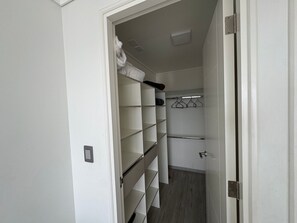 A walk-in closet with open shelves, a hanging rod, and a door leading to another room.