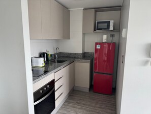 A compact kitchen with a microwave, toaster, sink, and a red refrigerator. - Edificio Stepke (Temuco)