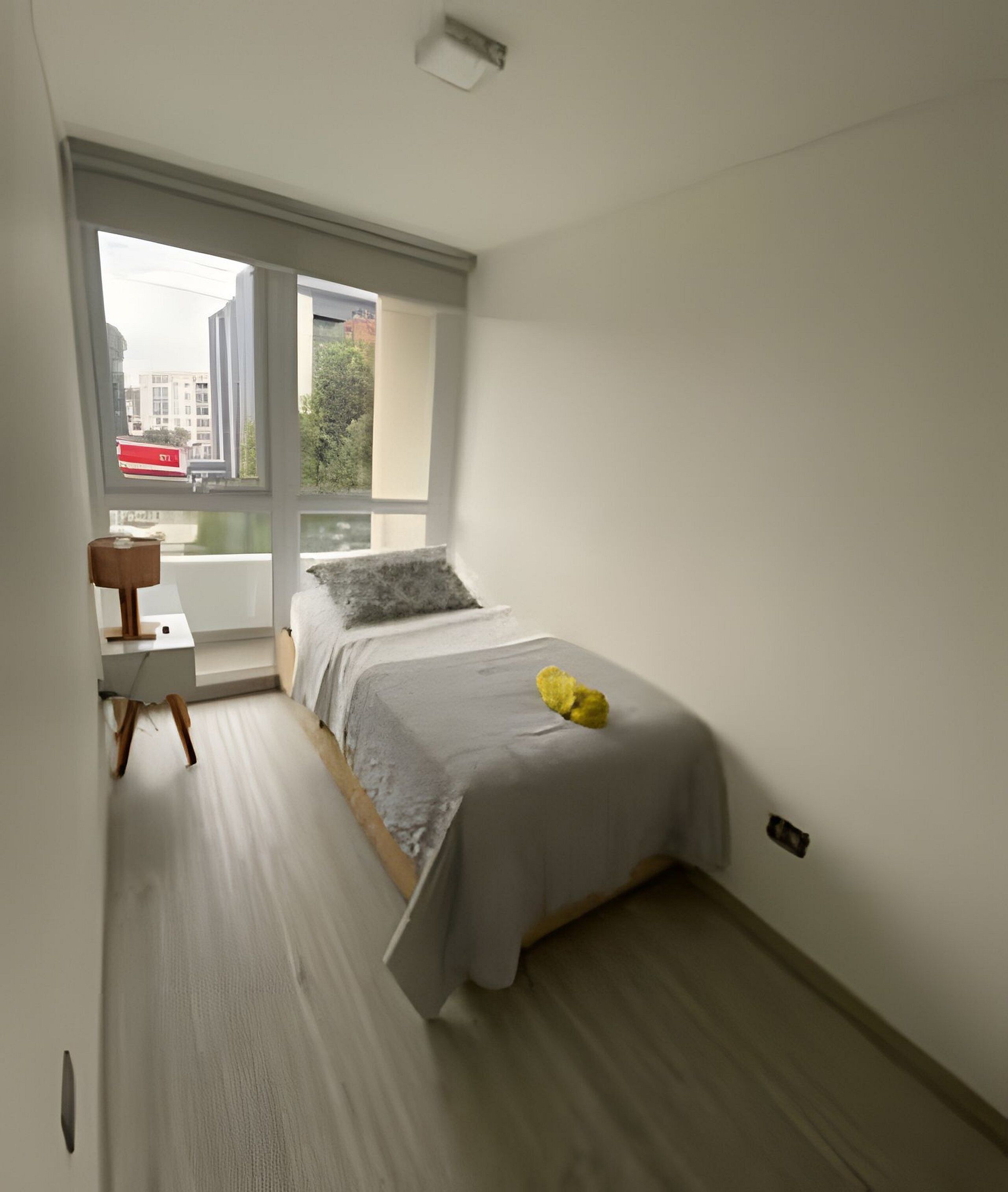 Ein kleines, modernes Schlafzimmer mit einem Bett, einem Sessel und einem großen Fenster mit Blick auf die Stadt.