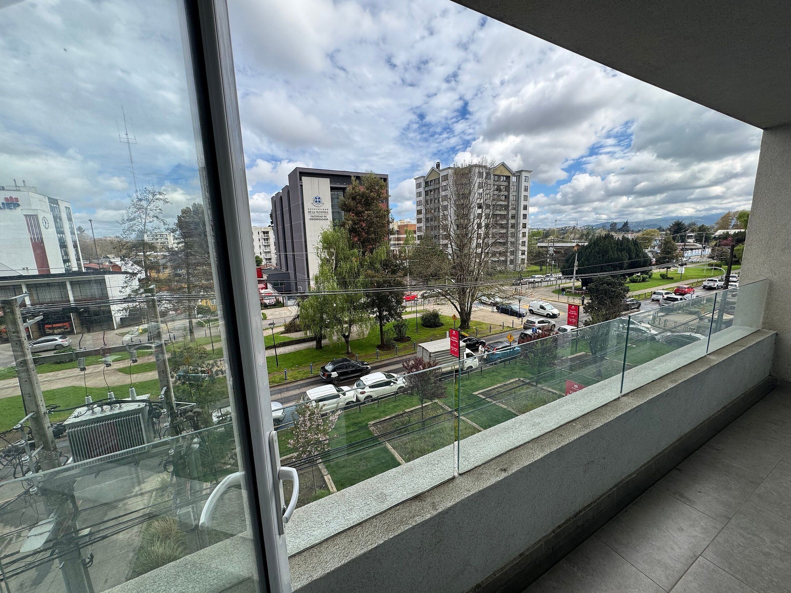 Vista desde un balcón sobre un estacionamiento y edificios, incluyendo una estructura alta con un letrero.