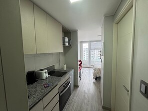 A compact kitchen with a toaster, microwave, and a small dining area with a chair. - Edificio Stepke (Temuco)