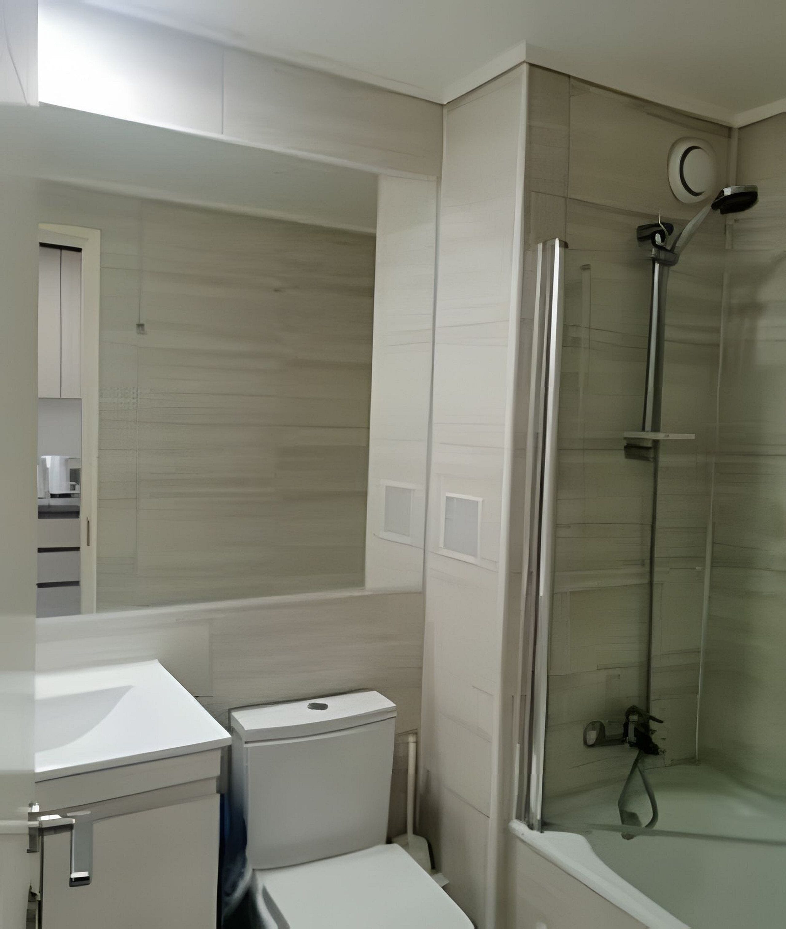 Un baño moderno con inodoro, lavamanos y ducha con mampara de vidrio.
