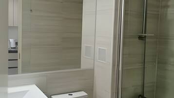 Un baño moderno con inodoro, lavamanos y ducha con mampara de vidrio.