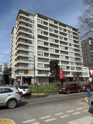 Un edificio residenziale a più piani con balconi, un negozio ben visibile e auto parcheggiate lungo la strada.