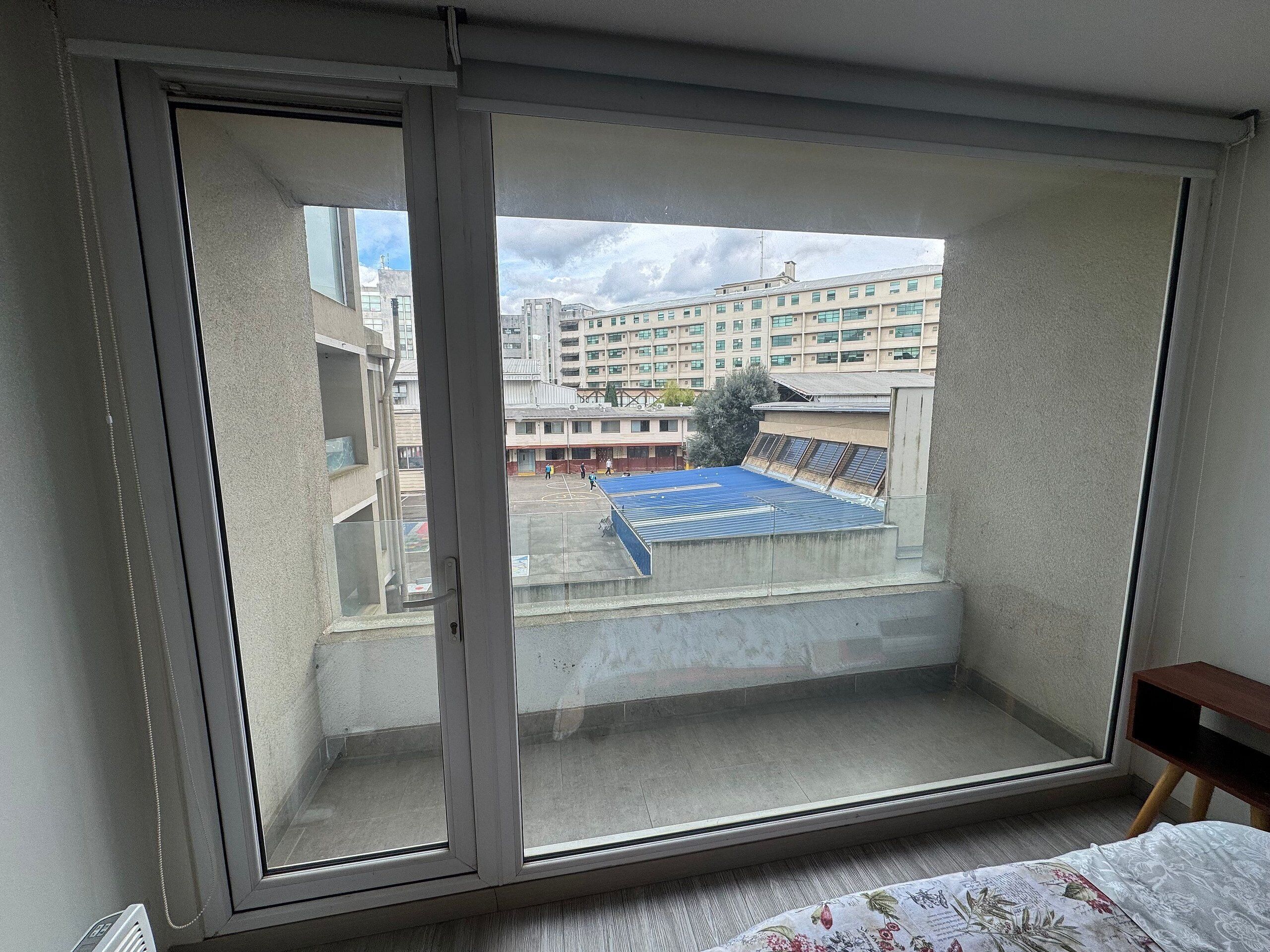 Una habitación con un ventanal grande que da a una cancha deportiva y un edificio de varios pisos.