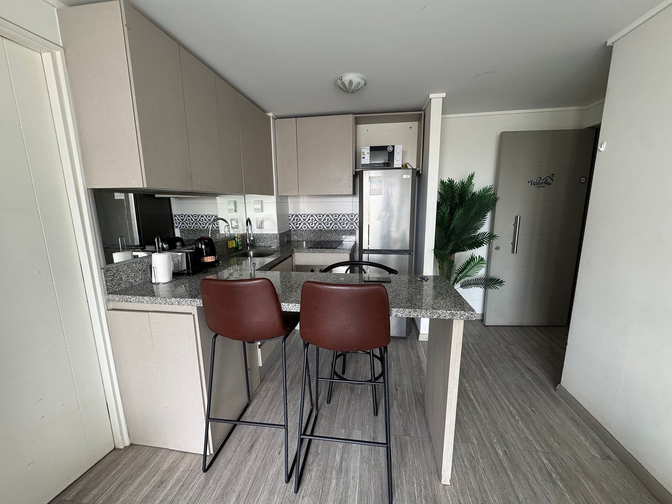 Cocina compacta con dos taburetes de bar, un microondas y un refrigerador.