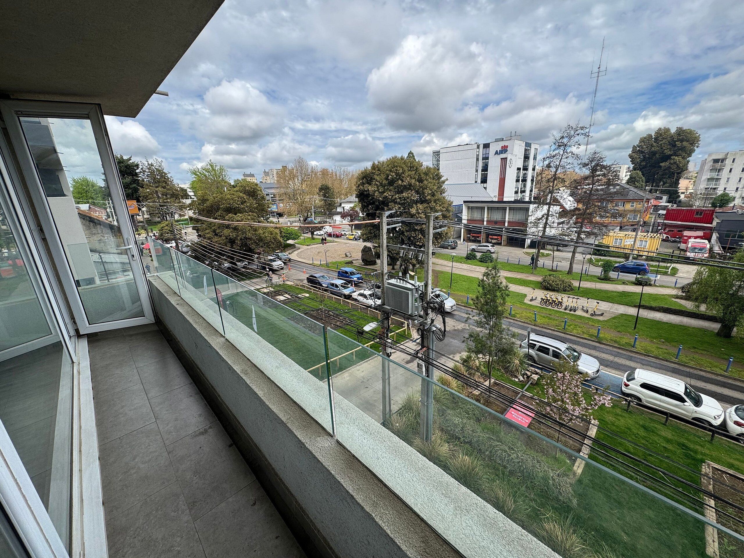 Un balcón con vistas a una calle de la ciudad, que incluye coches, edificios y un parque.
