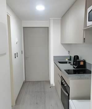 Una cocina compacta con una puerta blanca, una encimera con cafetera y un horno pequeño.