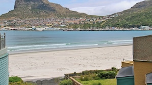 Une ville côtière dominée par une montagne imposante, dotée d’une plage de sable et d’un port de plaisance où sont amarrés des bateaux.
